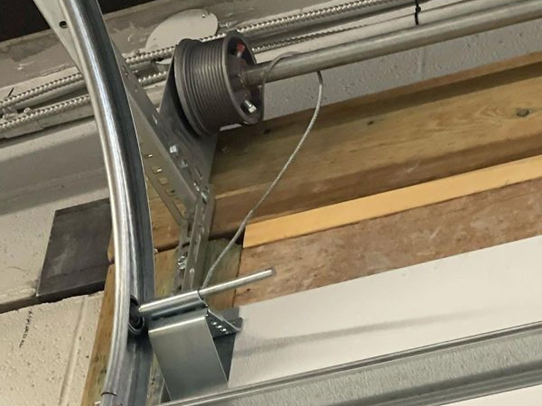 Lift cable and cable drum at the top corner of a garage door, the cable unseated from its drum and hanging slack down to the bottom bracket