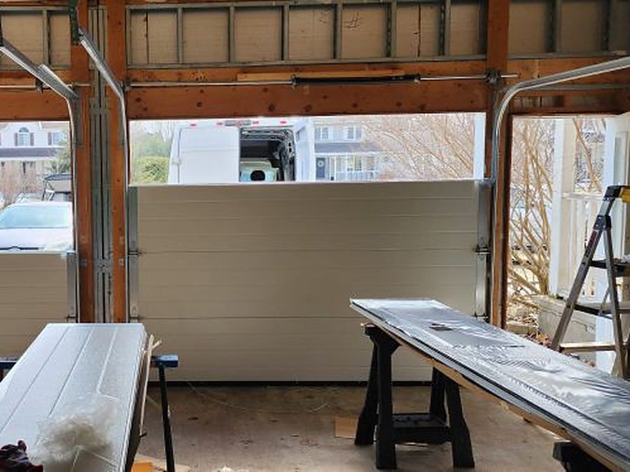 Two new insulated garage doors part-way through installation, with the remaining sections staged on trestles ready to be fitted