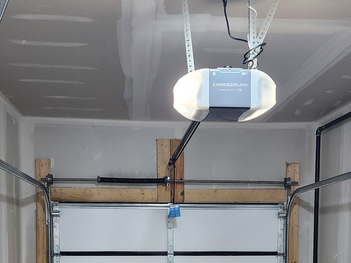 Garage door opener installed on a garage ceiling with wall-to-ceiling mounting brackets, the rail and door arm connected to the top section